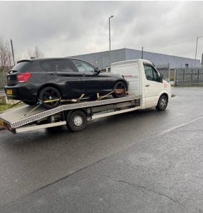 Black coupe secured on a flatbed recovery truck in an industrial area