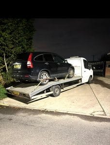 Black SUV loaded onto a flatbed recovery truck during a night-time recovery