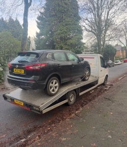 Black SUV secured on a flatbed recovery truck on a residential street