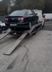 Black saloon being loaded onto a flatbed recovery truck with ramps extended