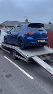 Blue hatchback on a recovery truck with loading ramps down