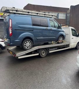Blue van secured on a flatbed recovery truck for commercial vehicle recovery
