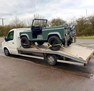 Classic green 4x4 vehicle loaded onto a flatbed recovery truck