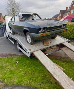 Classic green car being loaded onto a flatbed recovery truck using long ramps