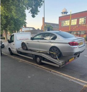 Grey saloon car loaded onto a flatbed recovery truck on a city street