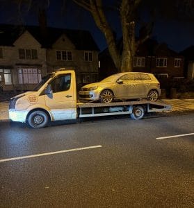 Saloon car loaded onto a flatbed recovery truck at night on a residential road
