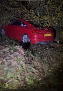 Red coupe off the road in bushes awaiting accident recovery at night