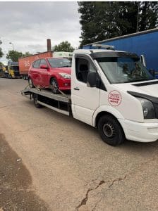 Red hatchback secured on a flatbed recovery truck in an industrial roadside location