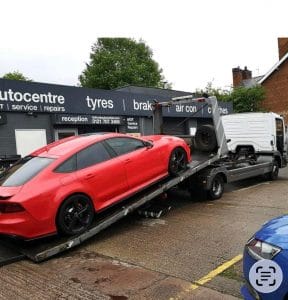 Red sports car loaded onto a recovery truck outside a tyre and repair shop