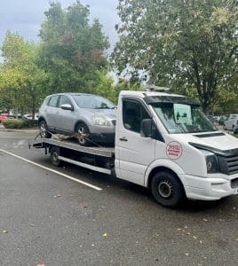 Silver SUV secured on a flatbed recovery truck in wet roadside conditions