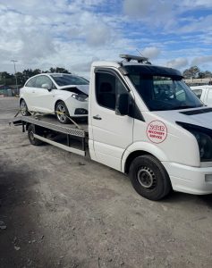 Silver SUV loaded onto a flatbed recovery truck in a roadside or depot setting