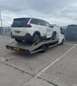White SUV secured on a flatbed recovery truck in a commercial yard
