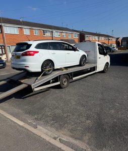 White SUV secured on a recovery truck at a commercial or roadside location