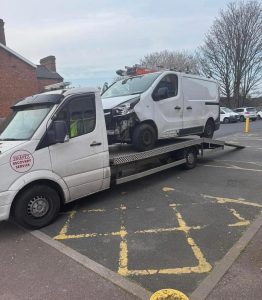 White van loaded onto a flatbed recovery truck in a marked car park