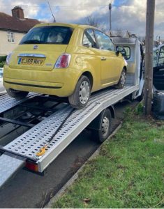 Yellow Fiat 500 loaded onto a flatbed recovery truck by the roadside