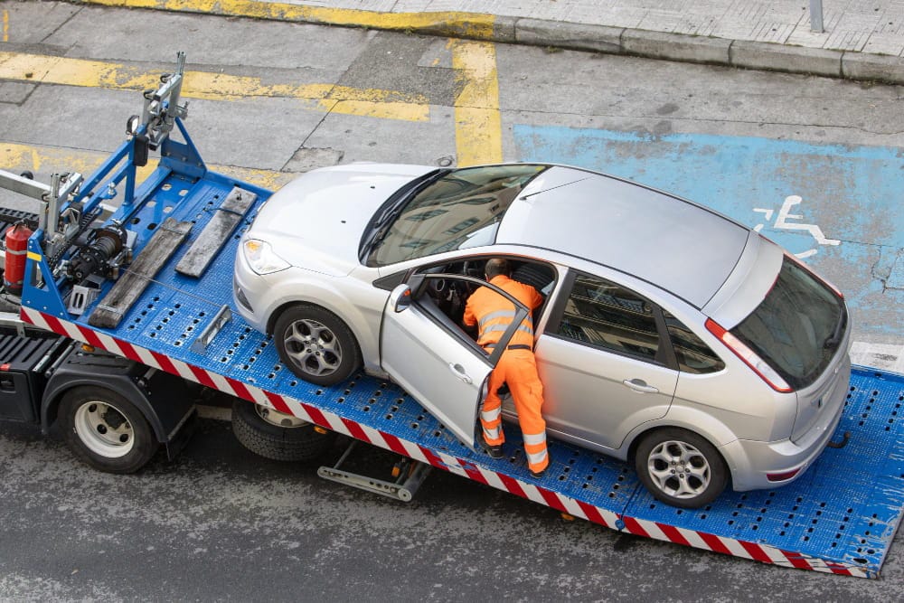 Worker secures a silver car during professional vehicle recovery works outdoors