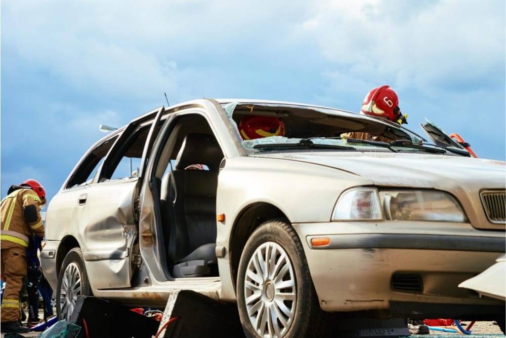 Firefighters perform vehicle extrication for accident recovery on a damaged silver sedan
