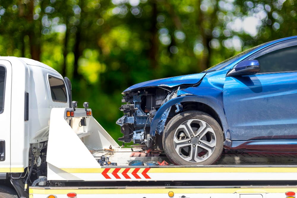 Damaged blue car transported on a flatbed for vehicle recovery services