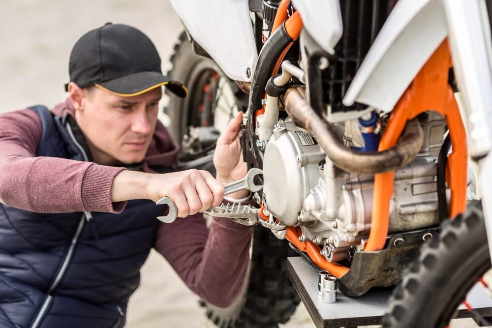 Technician performs motorbike breakdown recovery by repairing an engine with a wrench
