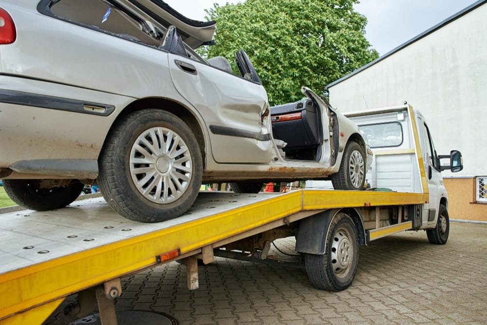 Flatbed truck delivers professional towing services Birmingham for a damaged silver sedan