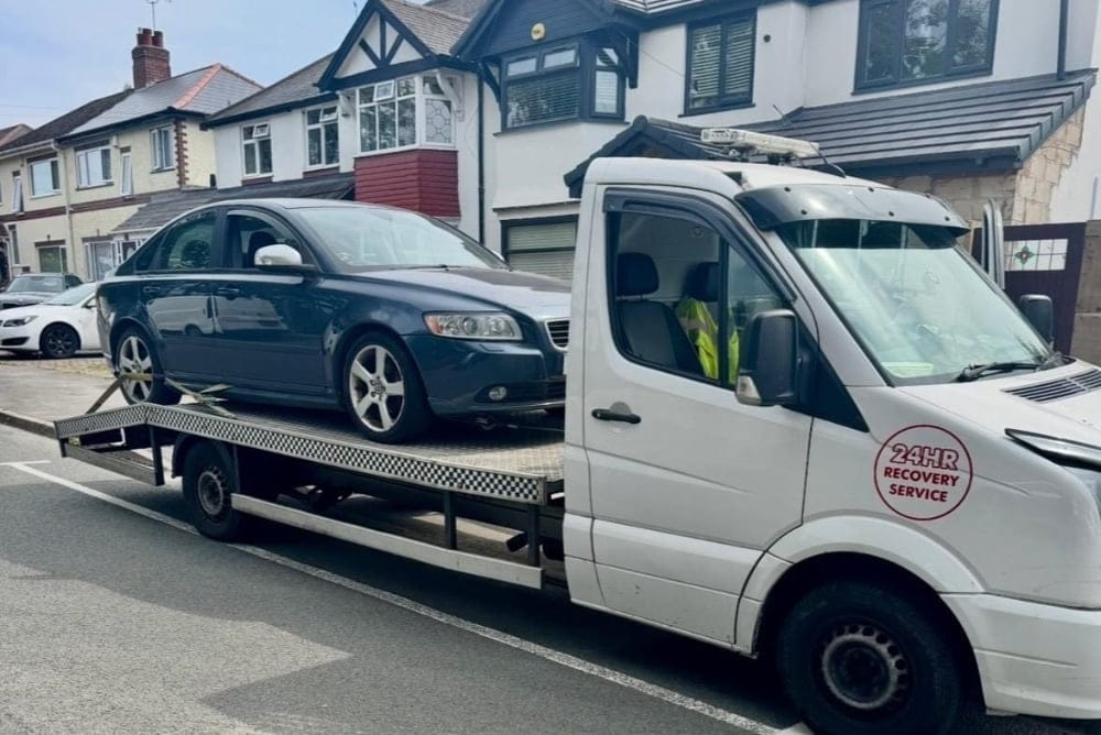 Efficiently providing reliable breakdown recovery services, a white flatbed tow truck transports a blue sedan