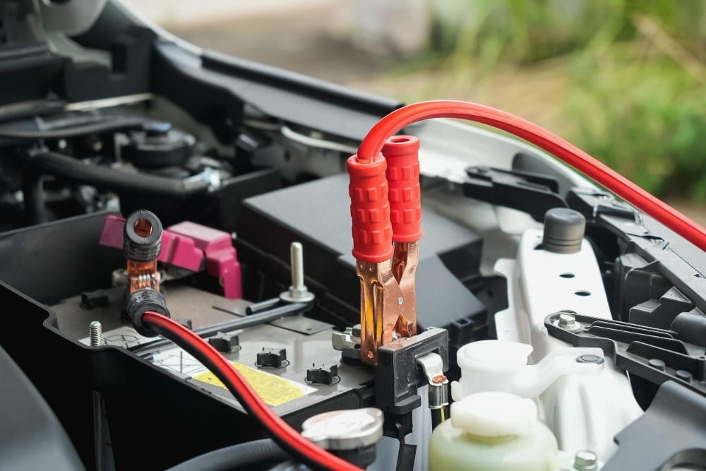 Red booster cables clamped onto a car engine for a battery jump start service