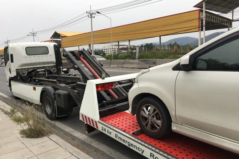 A white flatbed tow truck loads a disabled car for breakdown recovery