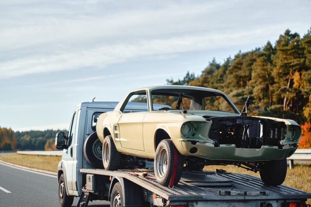 An old car chassis on a recovery truck undergoing scrap car collection