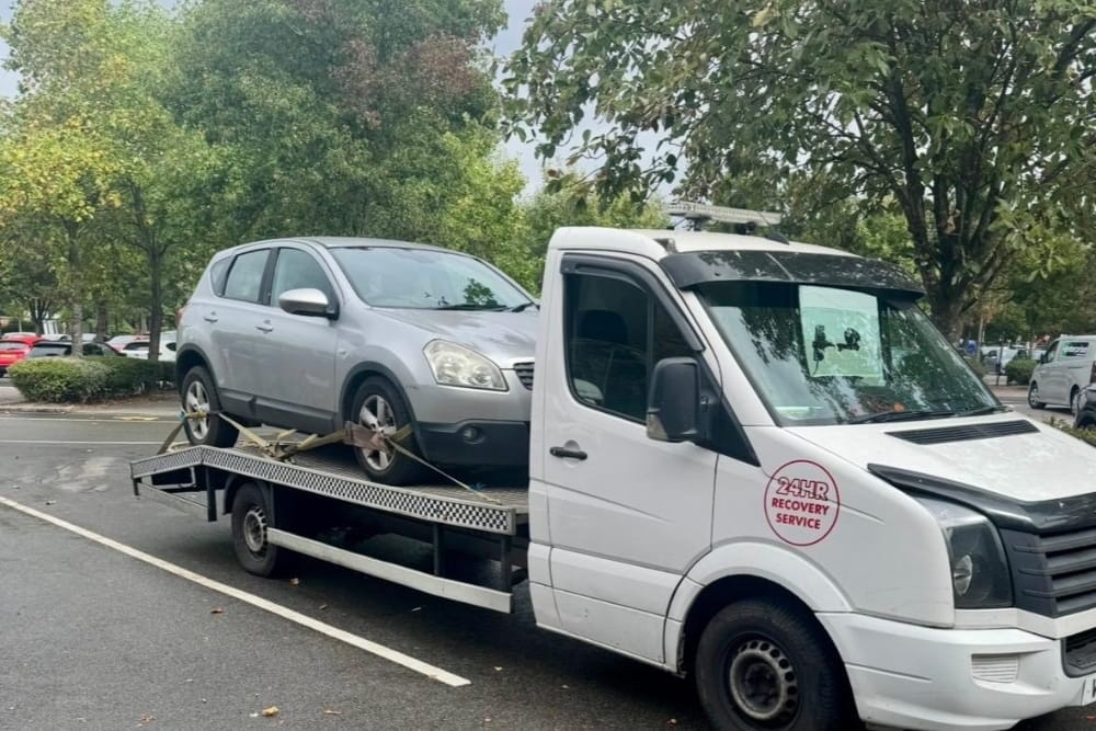 A white flatbed truck transports a silver SUV for car breakdown recovery