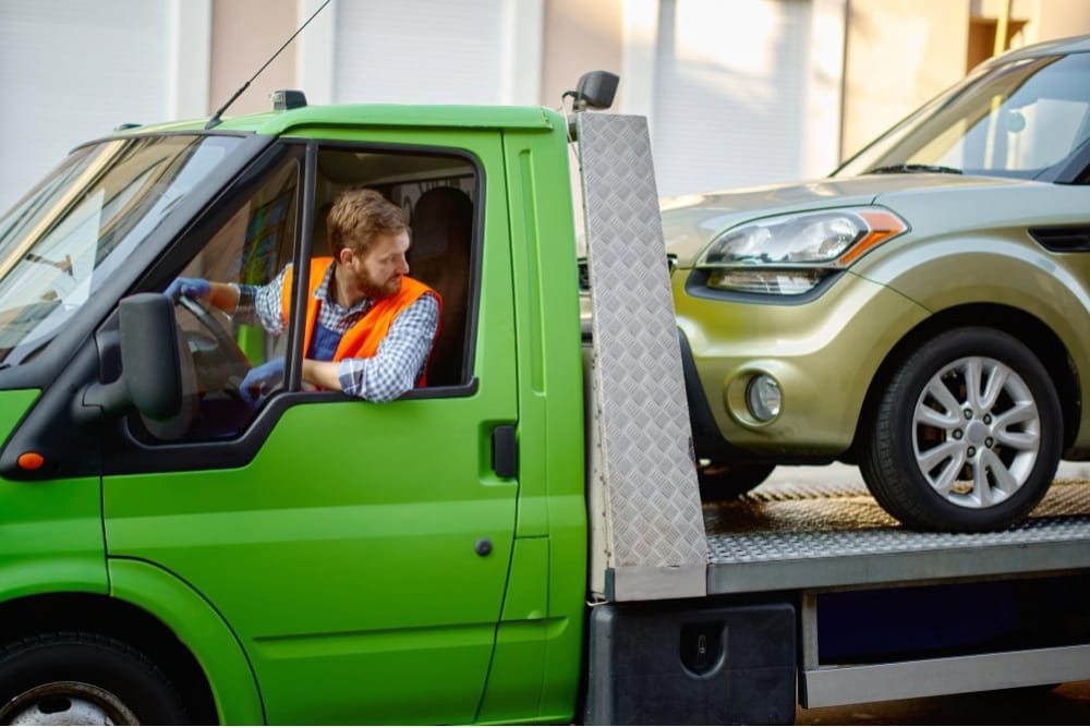 Tow truck driver utilizes van commercial vehicle recovery services to transport a gold car