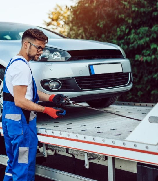 Tow truck driver loads silver car onto flatbed breakdown recovery truck