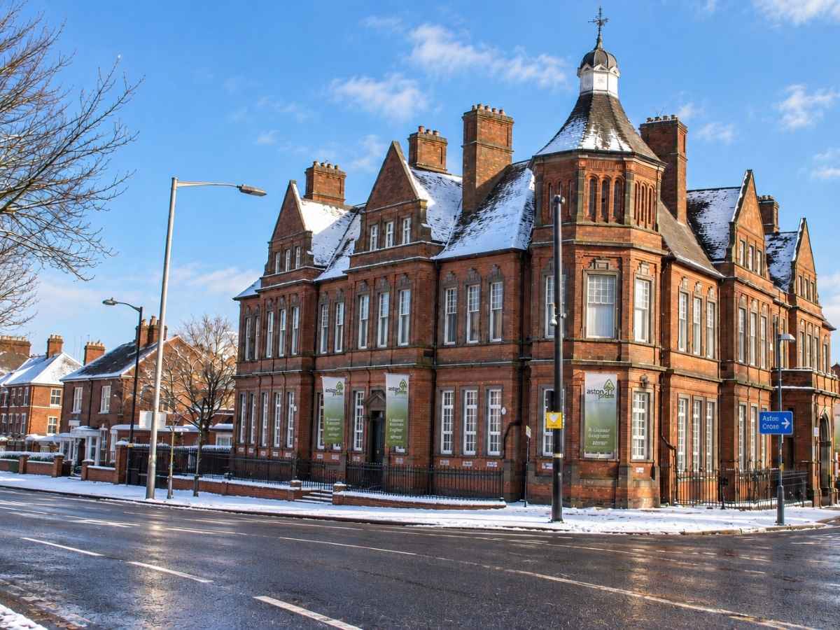 Snow-covered Aston Cross in Birmingham, showing a historic red-brick building and surrounding streets on a clear winter day