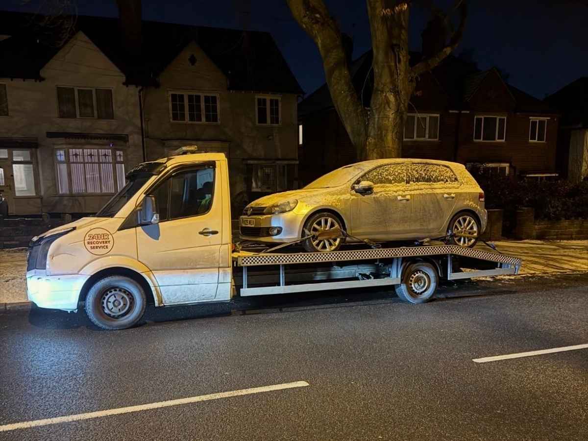 Nighttime flatbed tow truck providing 24-hour car breakdown recovery Aston for snow-covered hatchback
